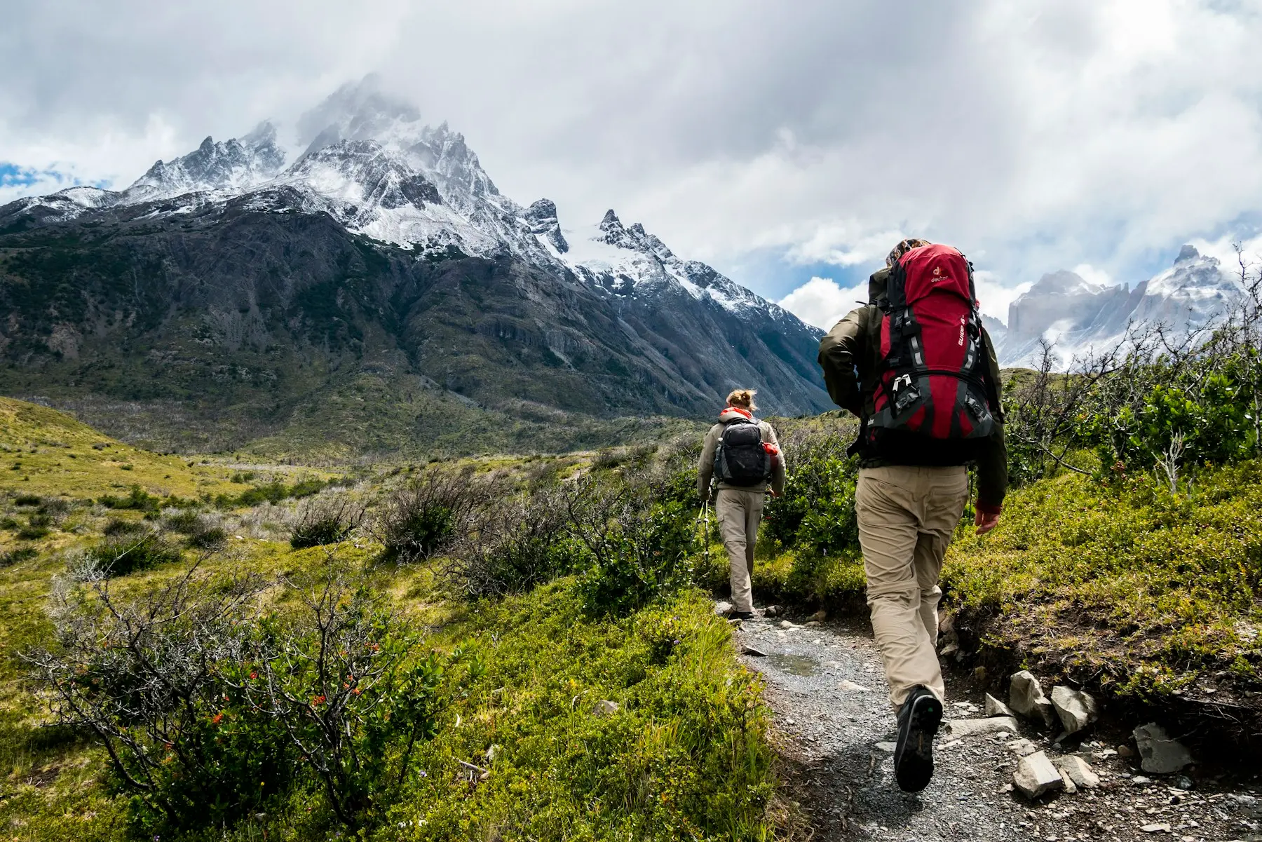 Two hikers walking a mountain trail with heavy backpacks