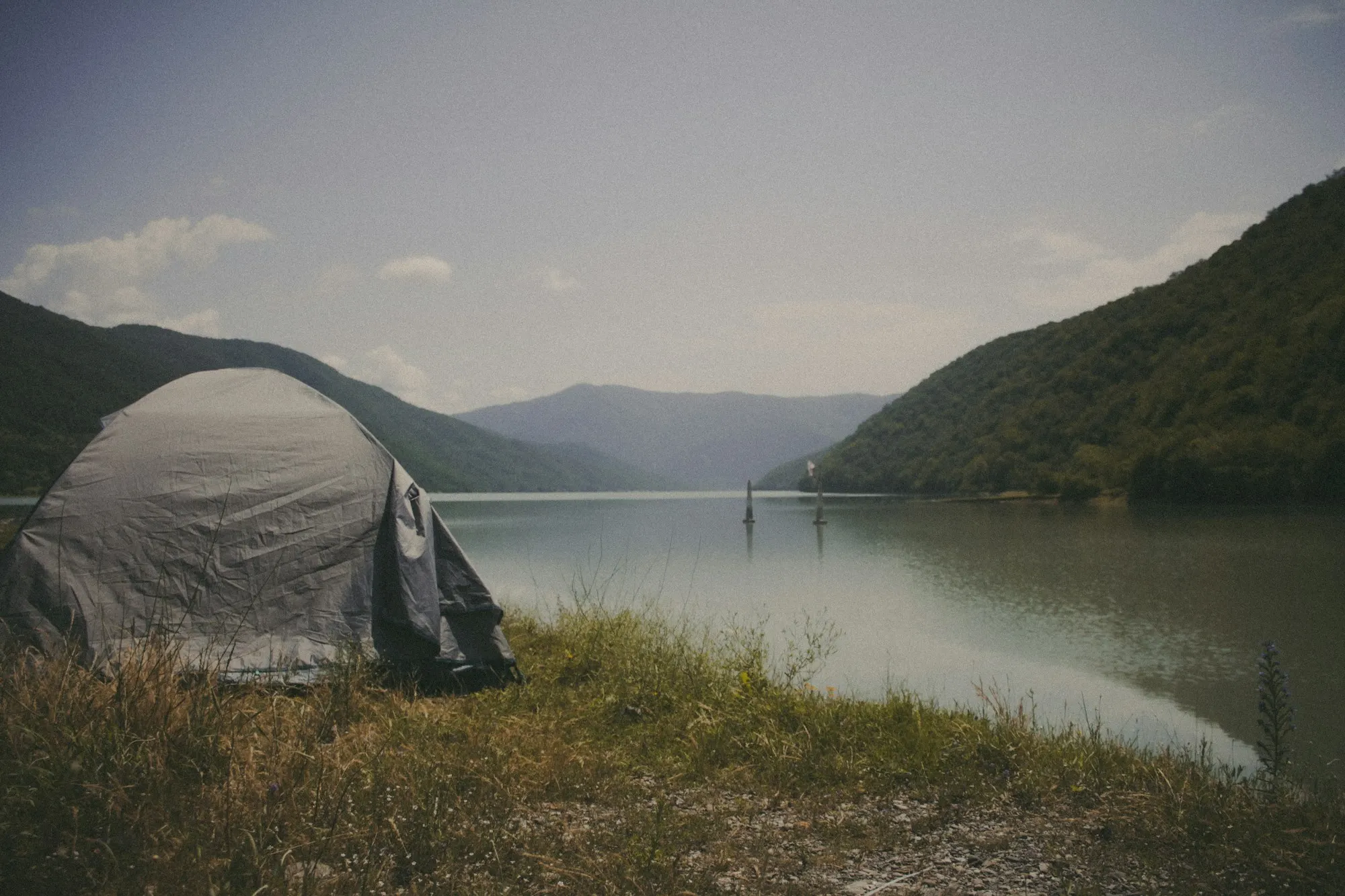 Grey tent pitched on the shore of a still mountain lake