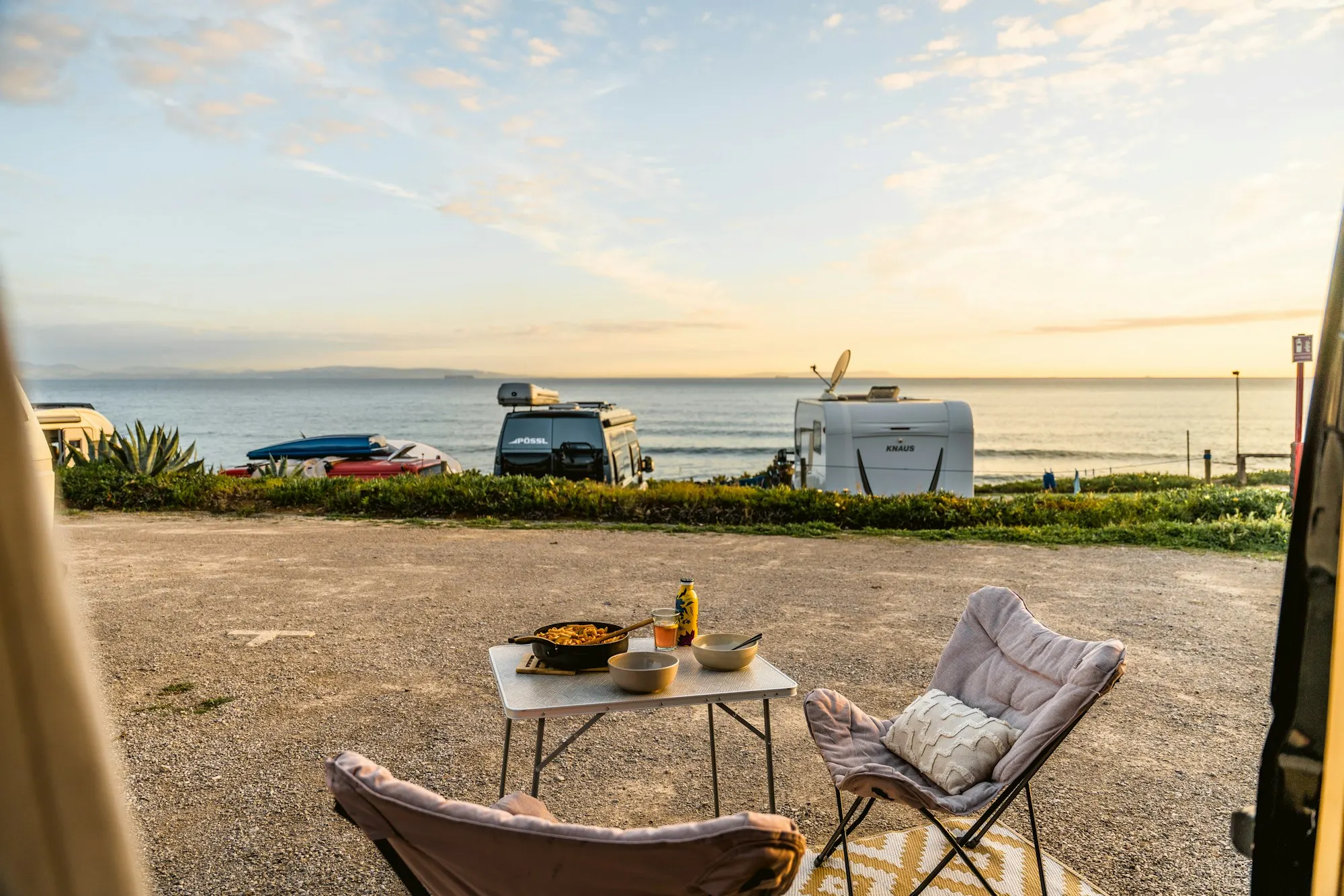 Campervans parked above the sea with a table set for dinner outside