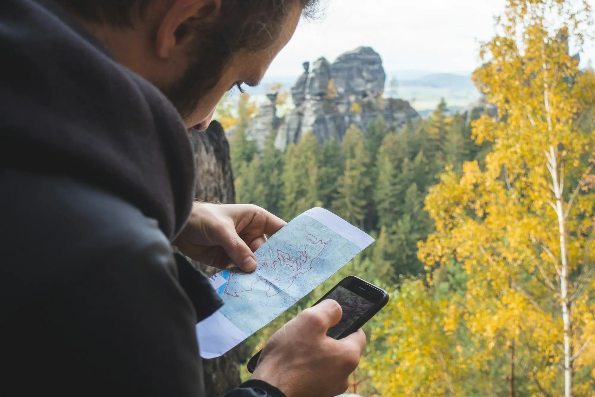 Traveller checking a paper map and a smartphone in autumn mountains