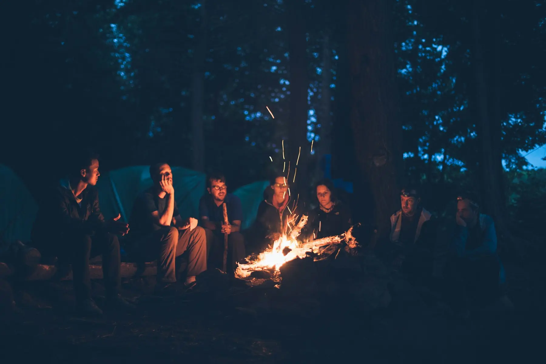 Group of friends gathered around a campfire at night