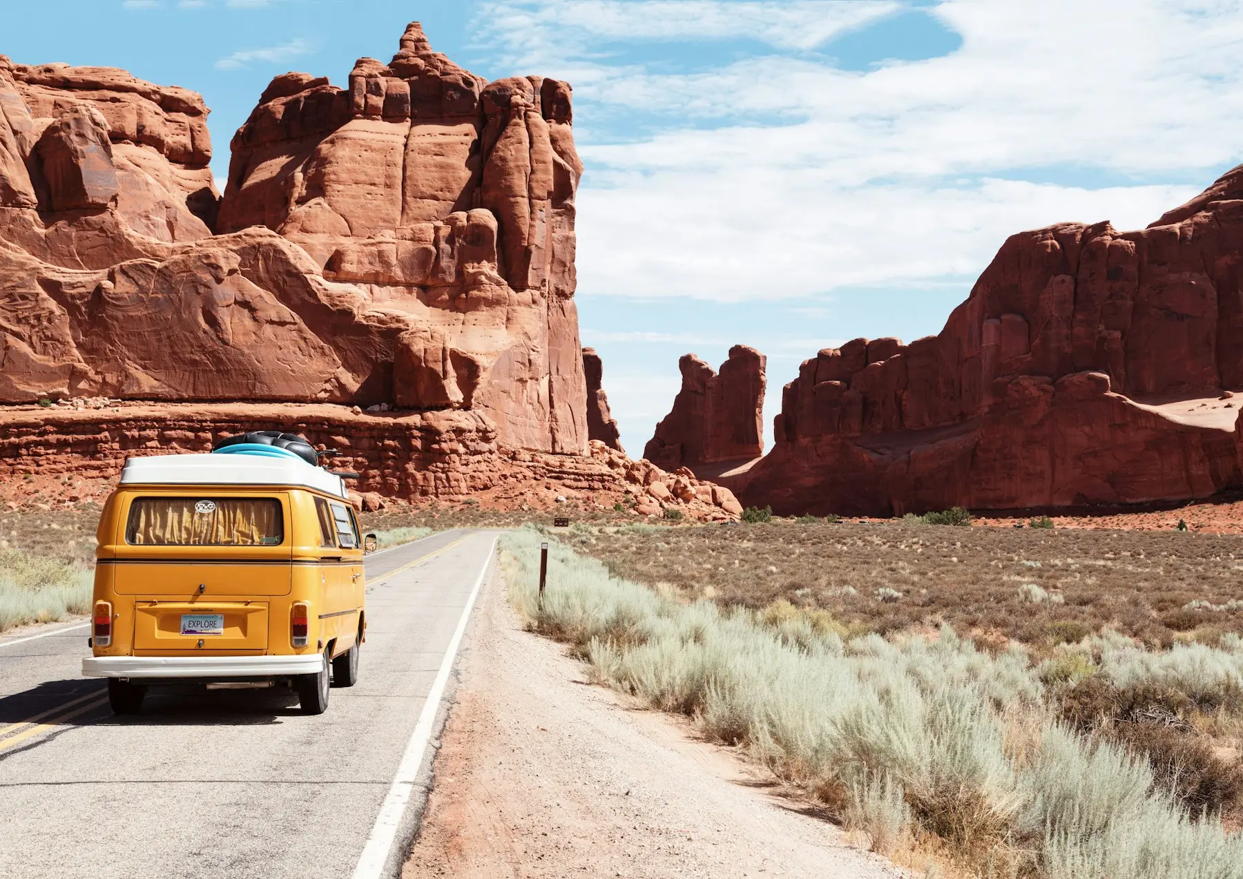 Yellow van driving a desert road between red rock cliffs