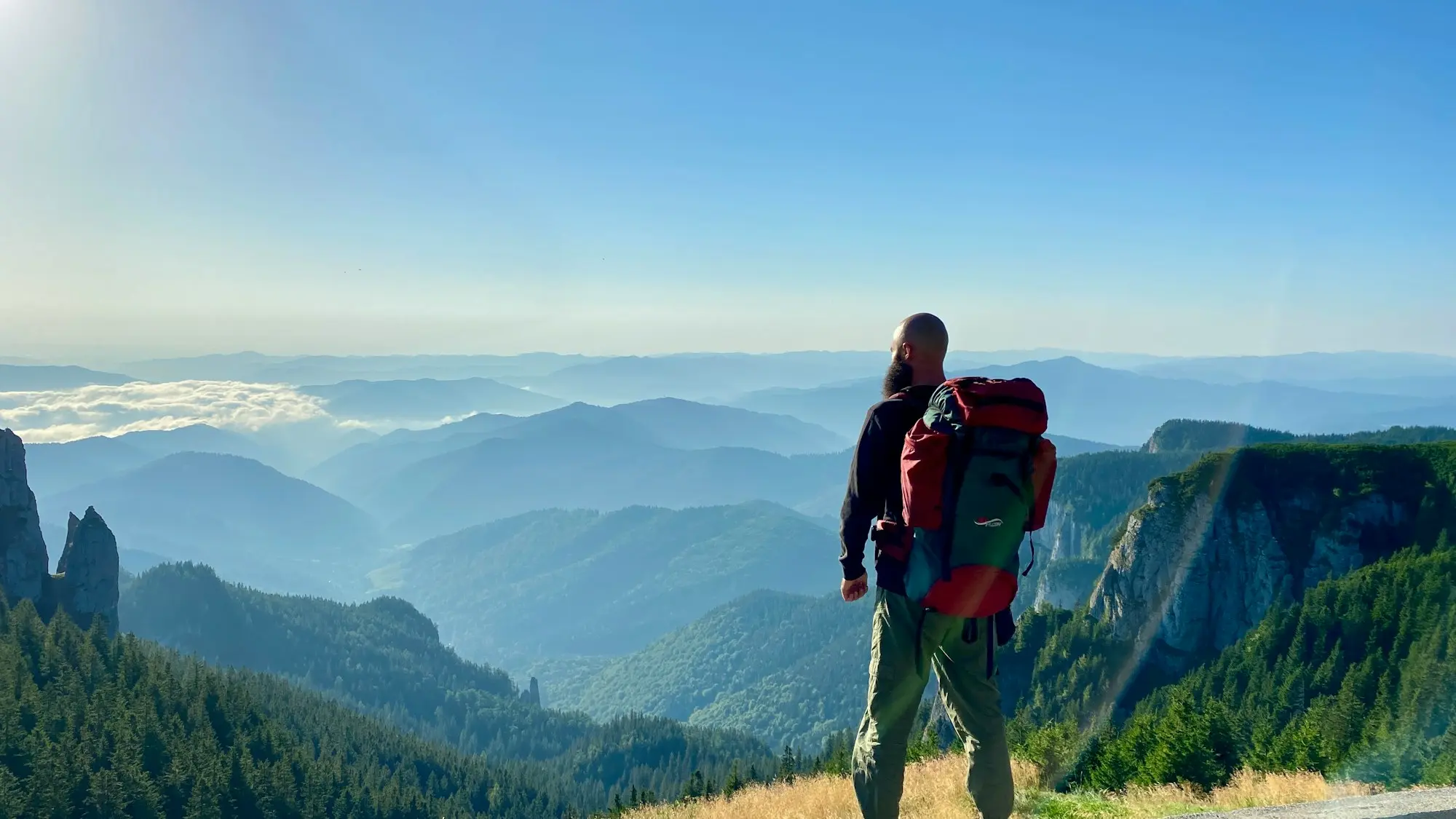 Hiker with a backpack on a summit above misty valleys