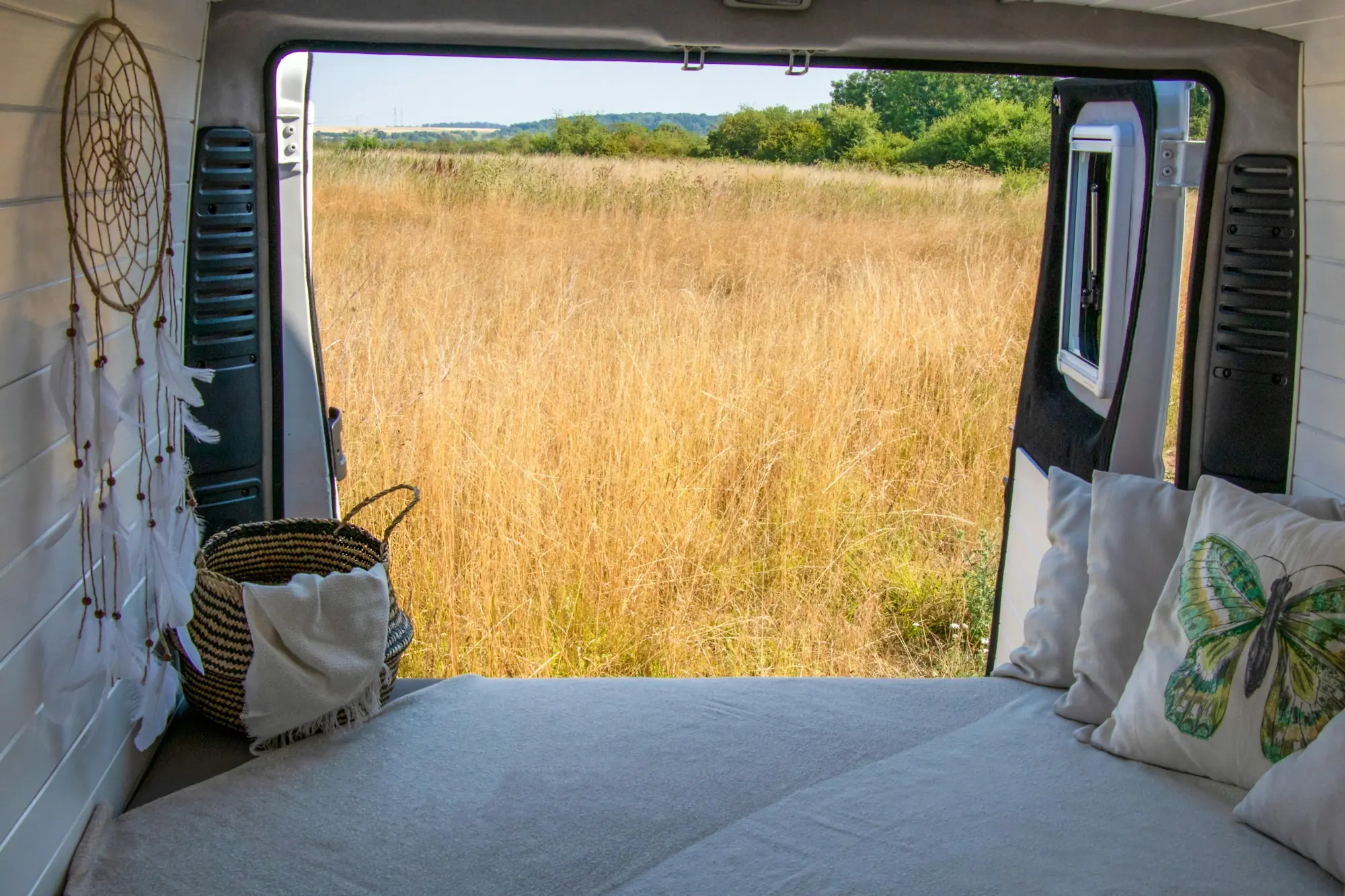 Campervan bed with the rear doors open onto a golden field